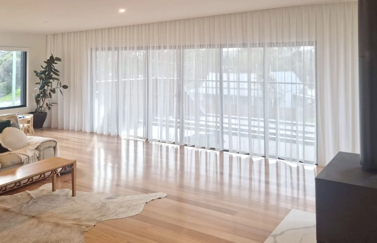 Sheer curtains drawn across a wall of windows in a light-filled living room