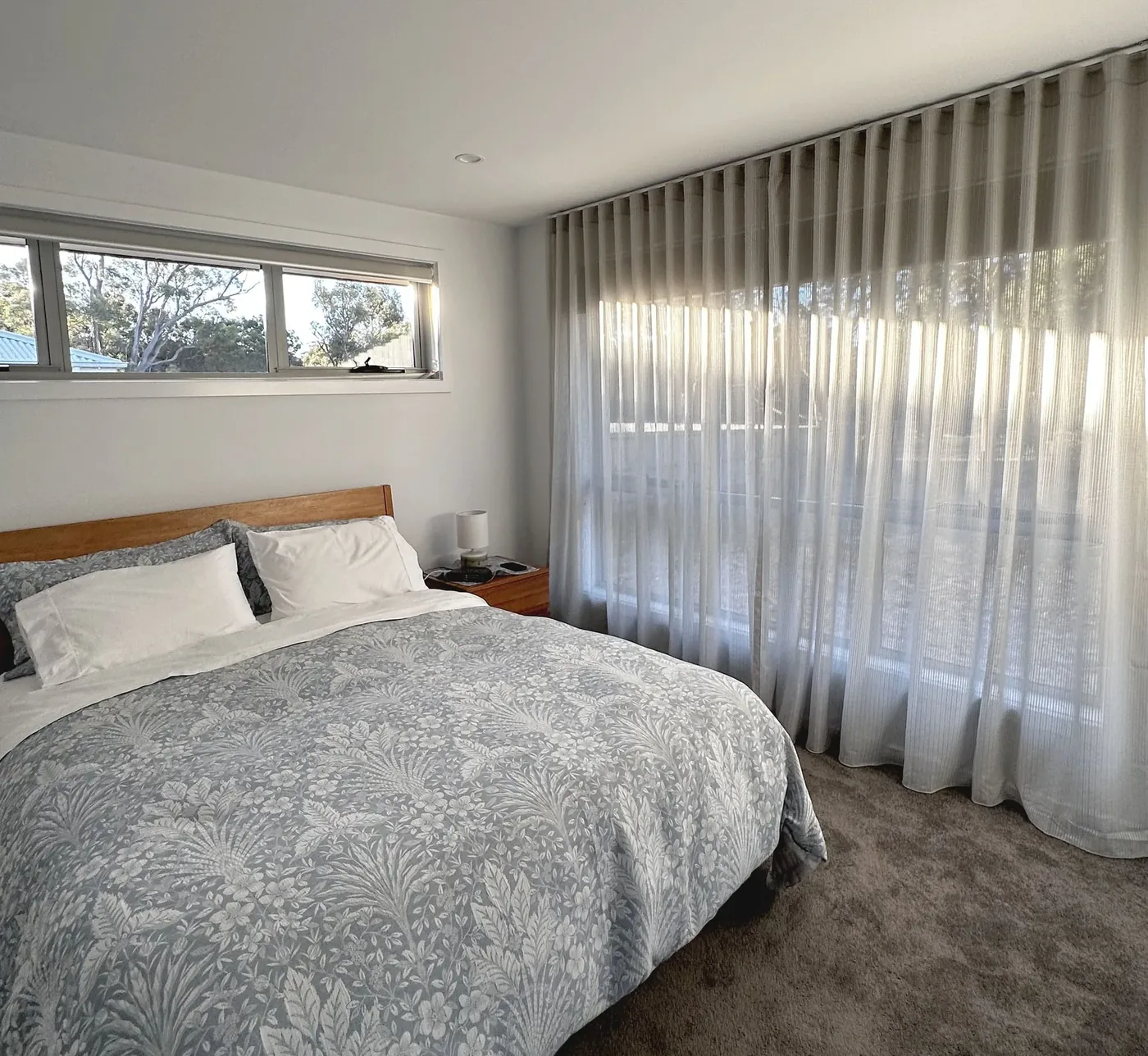 Sheer curtains drawn across a bedroom window beside the bed