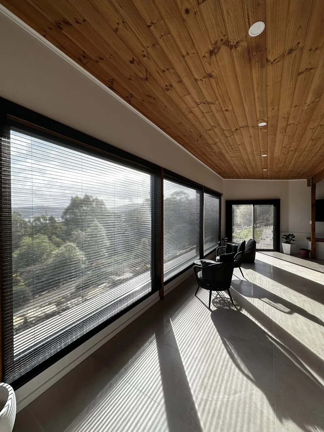 Pleated blind and sheer against a window under a timber ceiling