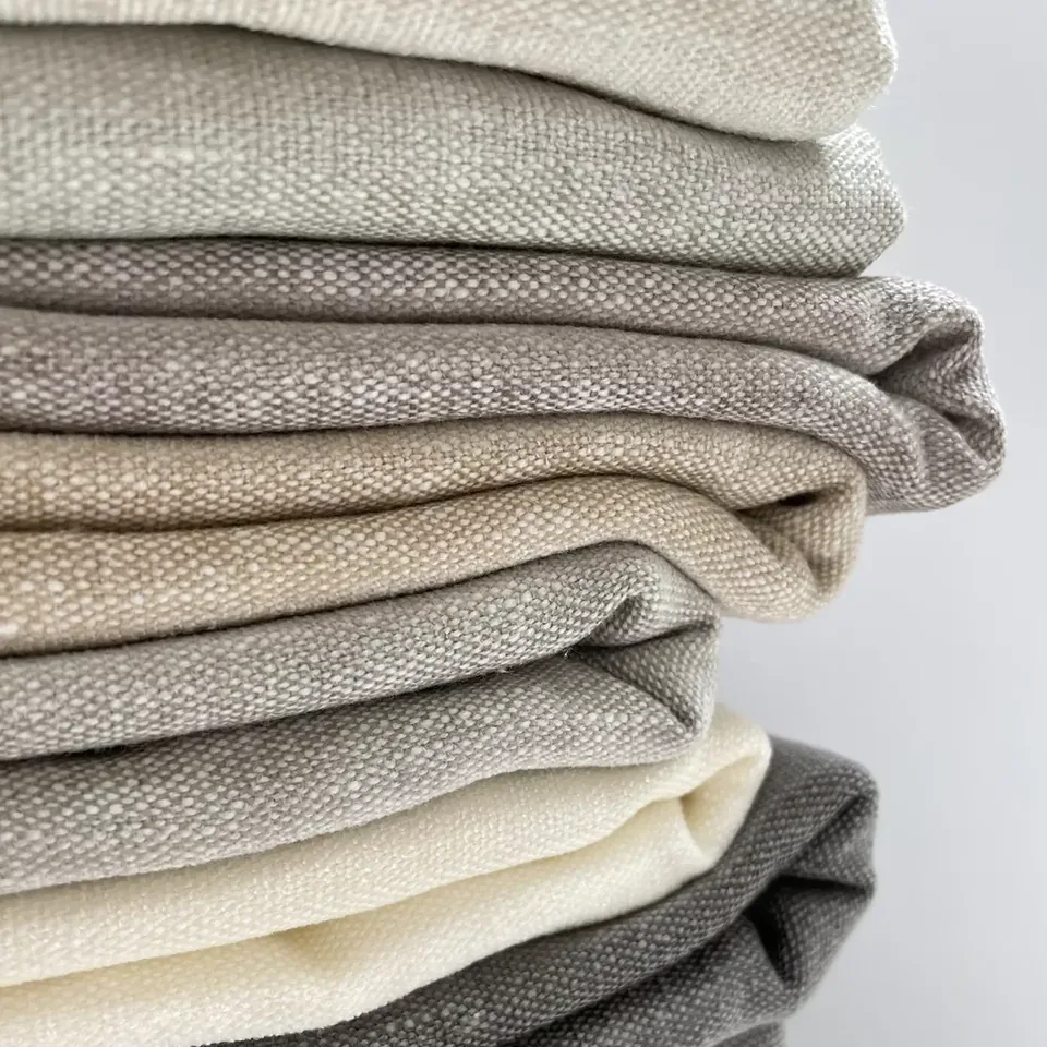 Folded stack of Aurelius curtain fabrics in ivory, oatmeal and charcoal