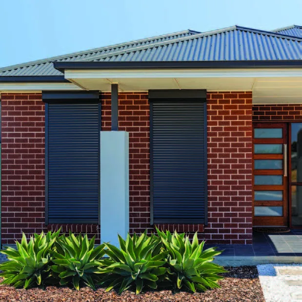 Outdoor roller shutters closed over the front windows of a brick home